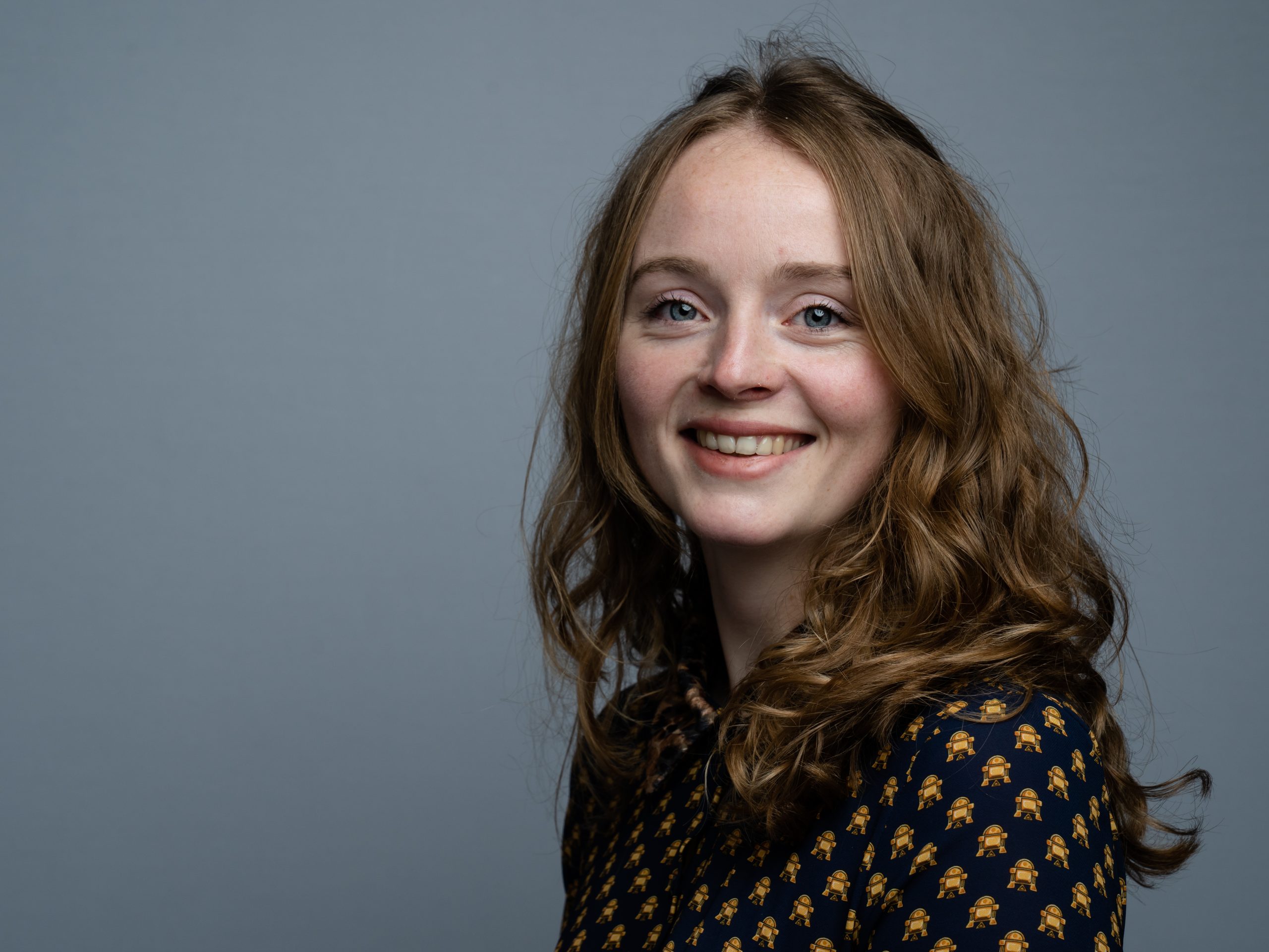 Portrait of a smiling woman with curly hair against a grey background.